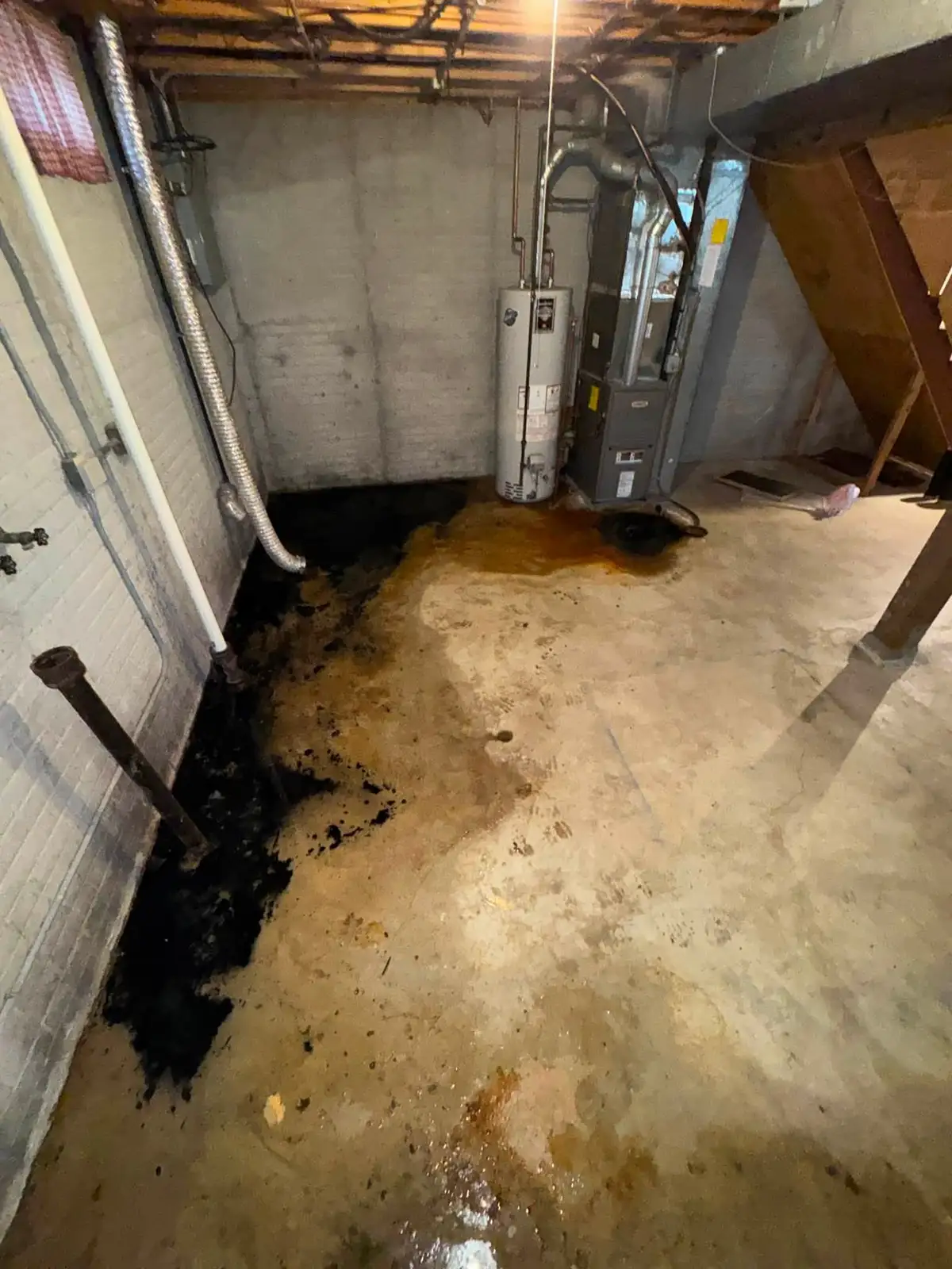 Water-damaged Scarborough basement before restoration, standing water and staining on the concrete floor by the furnace